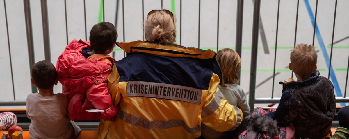 Eine Mitarbeiterin der Malteser betreut geflüchtete Kinder auf einer Tribüne in der Sporthalle. 