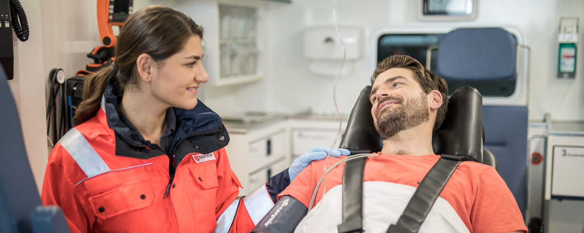 Eine Rettungssanitäterin lächelt einen Mann in einer Krankentrage an. 