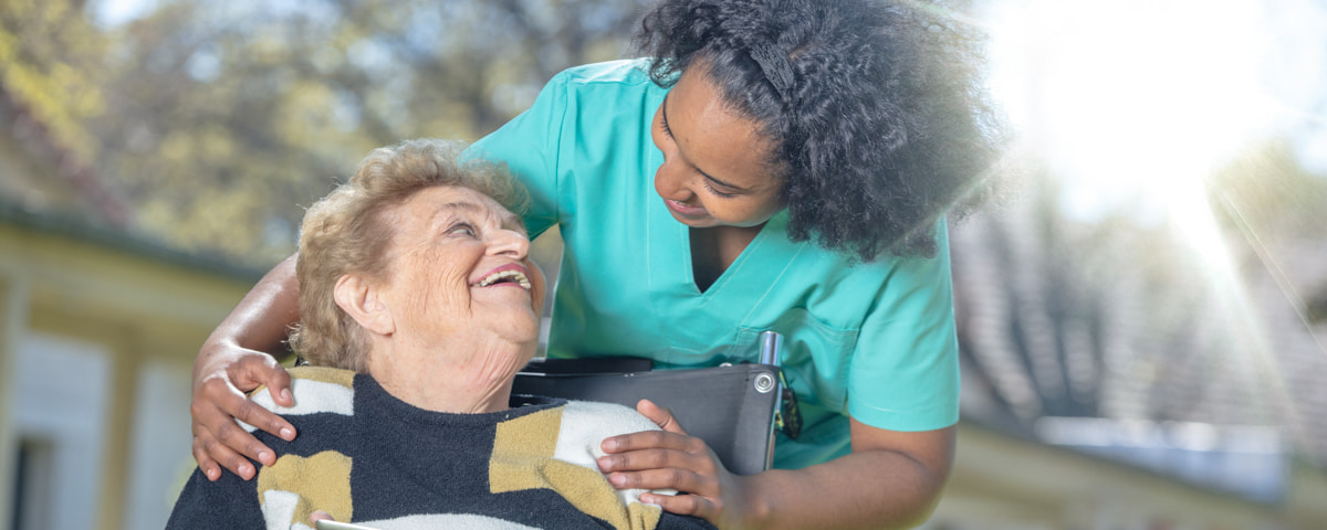 Eine Pflegerin der Malteser hilft einer älteren Frau im Rollstuhl.