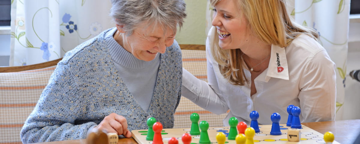Mitarbeiterin der Malteser Demenzbetreuung spielt mit einer älteren Frau ein Brettspiel.