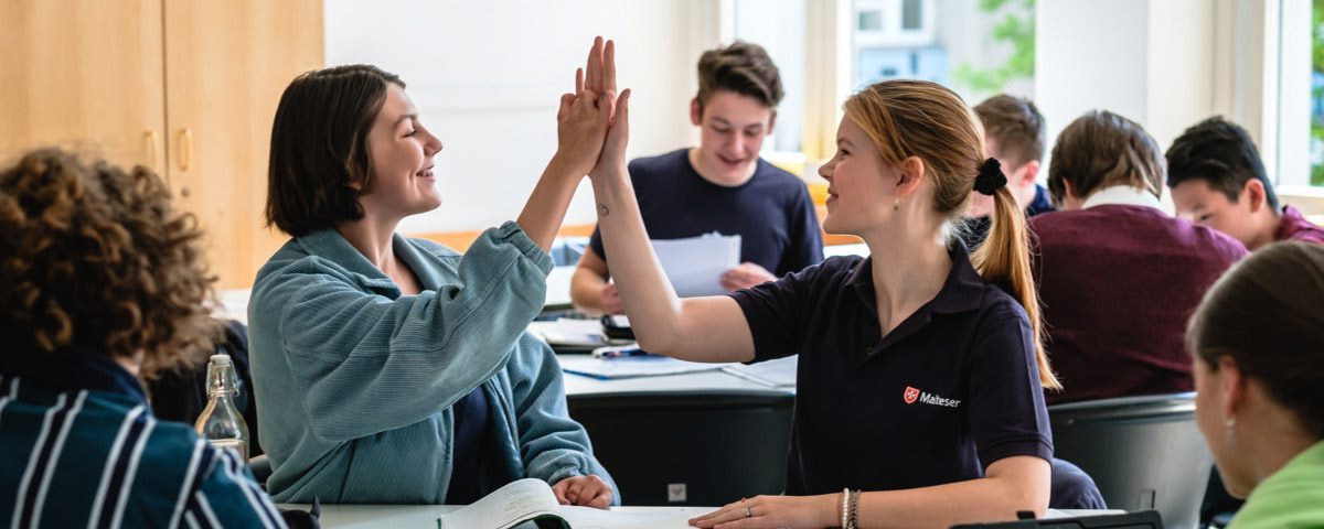 Zwei Malteser Mitarbeitende klatschen sich im Klassenraum ab. 